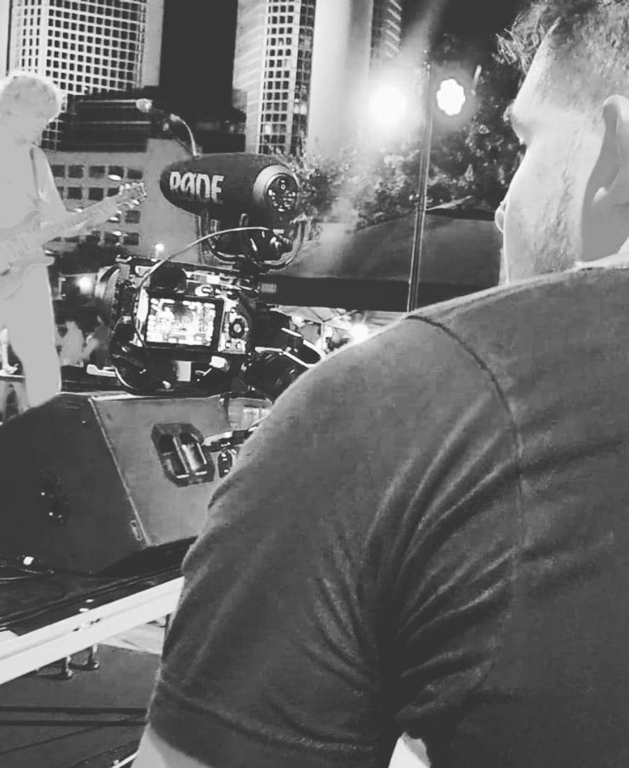 Black and white behind-the-scenes view of a live music performance being filmed by a professional camera operator